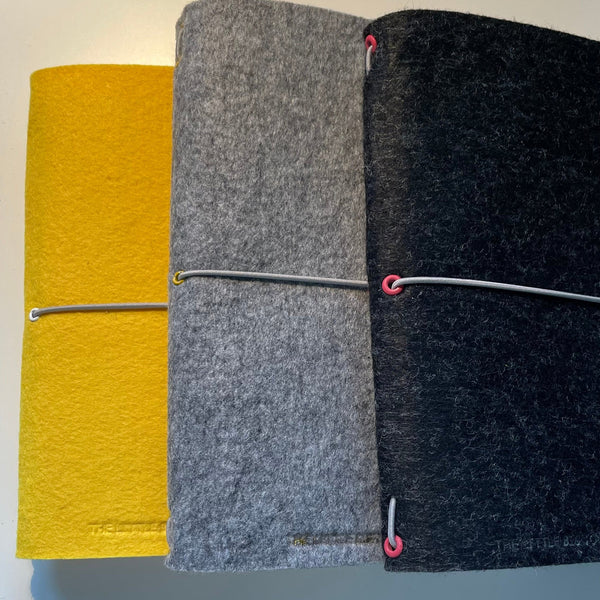 A selection of handmade A5 felt journals in bright yellow, silver grey and charcoal grey