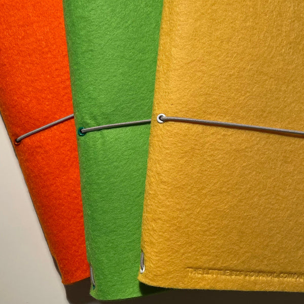 Bright orange, bright green and vivid yellow A5 felt journals fanned out to show colours