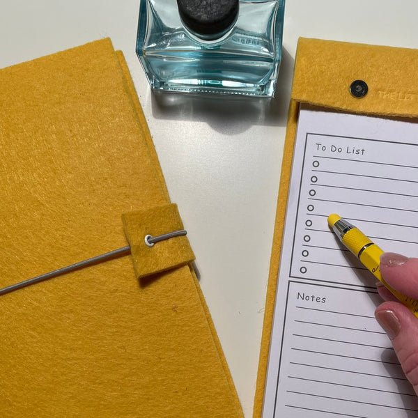Bright yellow felt journal and matching desk notepad sat on a desk with a pen and ink well