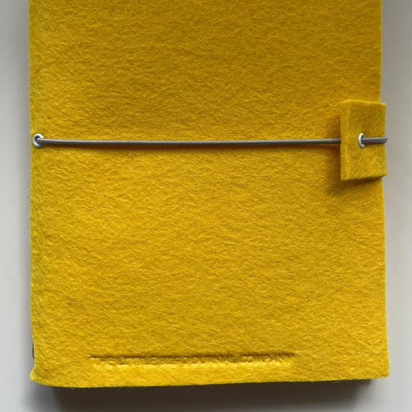 Bright yellow handmade felt  journal embossed with the little big journal company logo and elastic strap