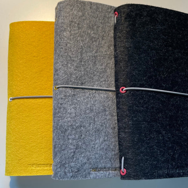 Bright yellow, silver grey and charcoal grey A5 felt wrap notebook, stacked to show the colour range