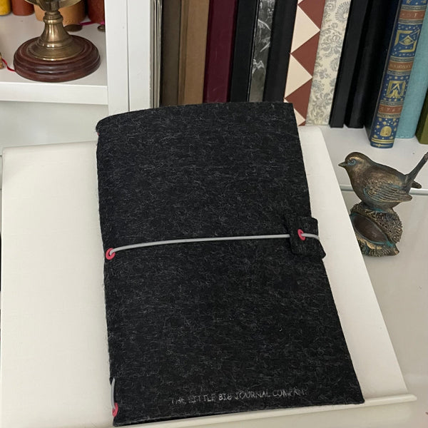 Charcoal grey felt journal wrap with elastic strap shown on study desk