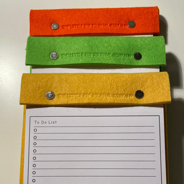 Orange, green and yellow A5 desk notepads stacked to show the range of colours