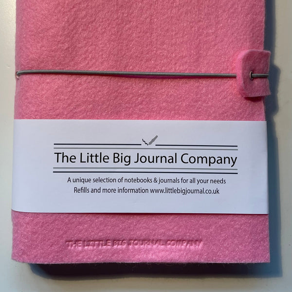 Pink felt wrap A5 refillable journal with elastic strap holding notebooks inside with packaging description