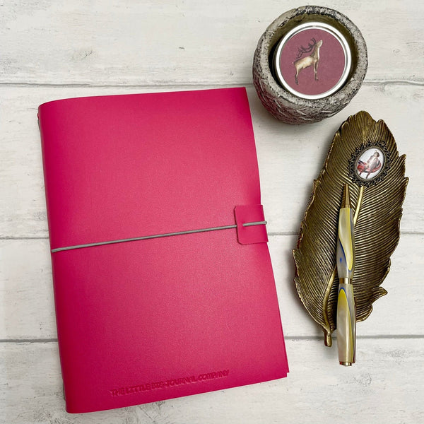 Pink pink A5 refillable soft faux leather journal notebook on a desk top with a pen and candle