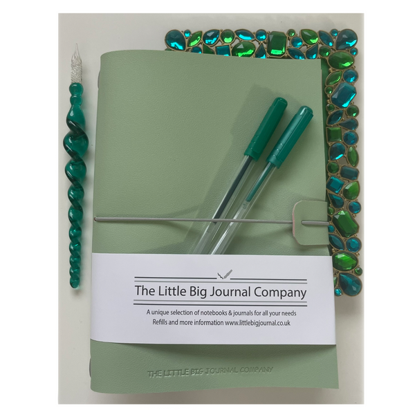green journal laying on desk with pens to show size