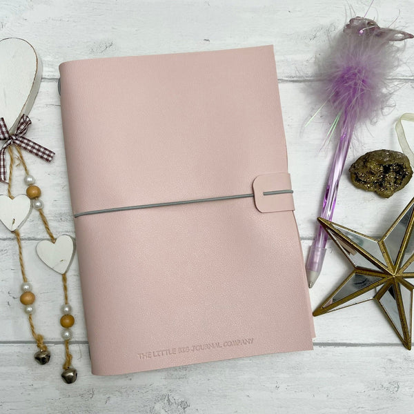 Soft pink A5 vegan leather journal with elastic strap on table with a pen and paperweight to show scale