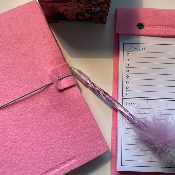 Pink felt wrap A5 refillable journal with elastic strap holding notebooks inside and a pink felt covered notepad with tear off pages for a to do list