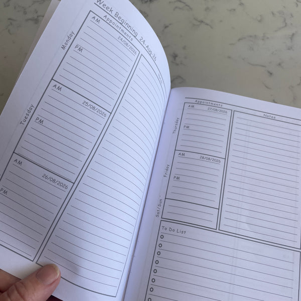 An open weekly planner spread showing lined pages with sections for weekday schedules, appointments, and a to-do list, held by a hand against a light marble surface.