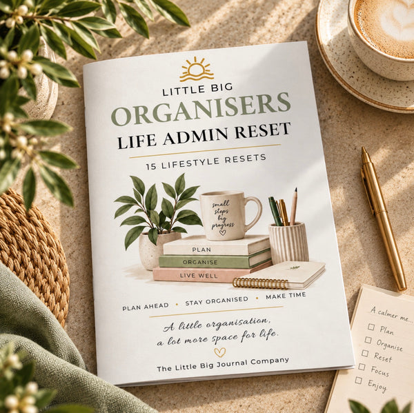 A book titled 'Little Big Organisers Life Admin Reset' is laid flat on a beige surface with styled office props, including a plant, mug, pencils, notebook, and coffee cup. The cover shows a white background with green and gold text and illustrations of books, a mug, and a plant.