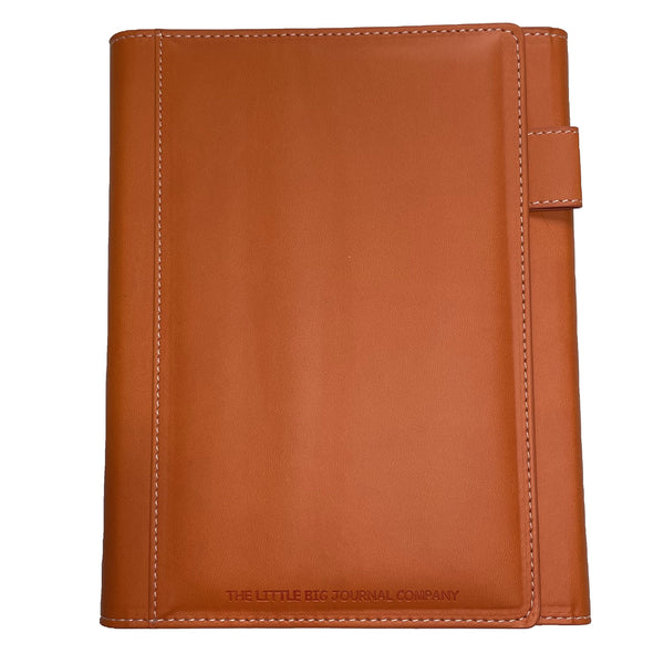 A burnt orange faux leather refillable journal with a magnetic clasp, displayed on a white background