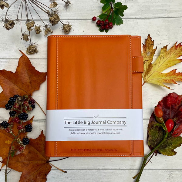 burnt orange faux leather refillable journal  showing on a background of autumn leaves showing how the colours compare.