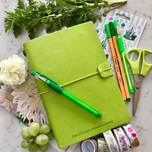 Blank Refillable Journal -Green with plain pages inserts. Picture shows the journal laying on desk  top surrounded by stationary items, pens etc